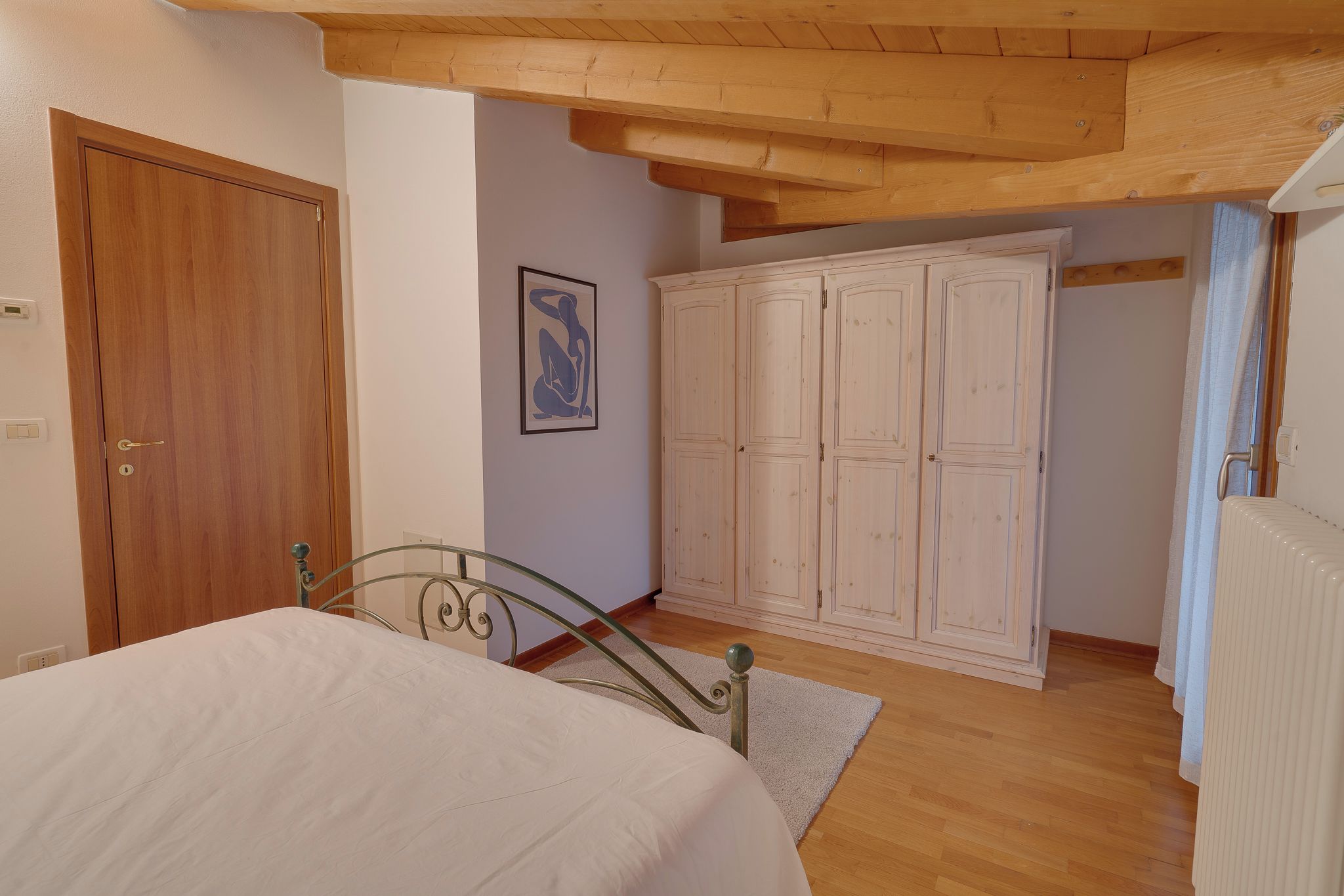 A bedroom with a bed, wardrobe, and a painting on the wall.