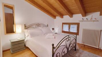 Un dormitorio con cama, mesita de noche, lámpara, ventana, radiador y vigas de techo de madera.