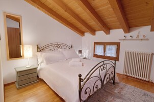 Un dormitorio con cama, mesita de noche, lámpara, ventana, radiador y vigas de techo de madera.