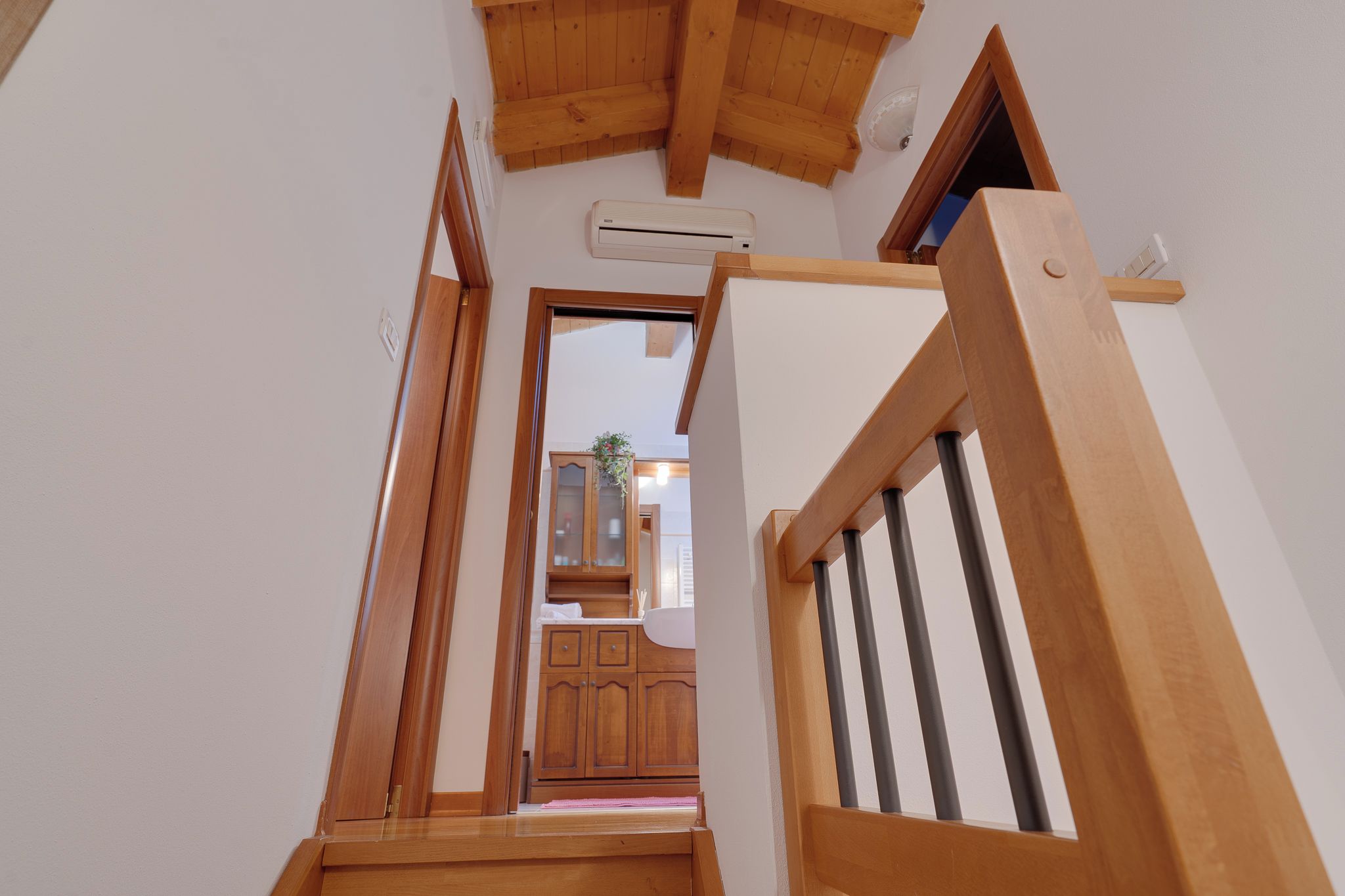 Un escalier en bois mène à une pièce dont le plafond est également en bois et dont un des murs est blanc.