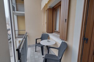 Un balcón con dos sillas, una mesita y una ventana con contraventanas de madera, además de una barandilla de metal.
