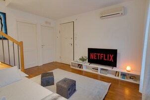 Una sala de estar moderna con un televisor de pantalla plana, una escalera y un pasillo que conduce a una puerta.