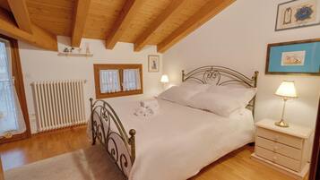 Un dormitorio con cama, mesitas de noche, radiador, ventana con cortinas y decoración en la pared.