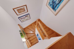 Una escalera de madera con barandilla, una planta y cuadros en las paredes.