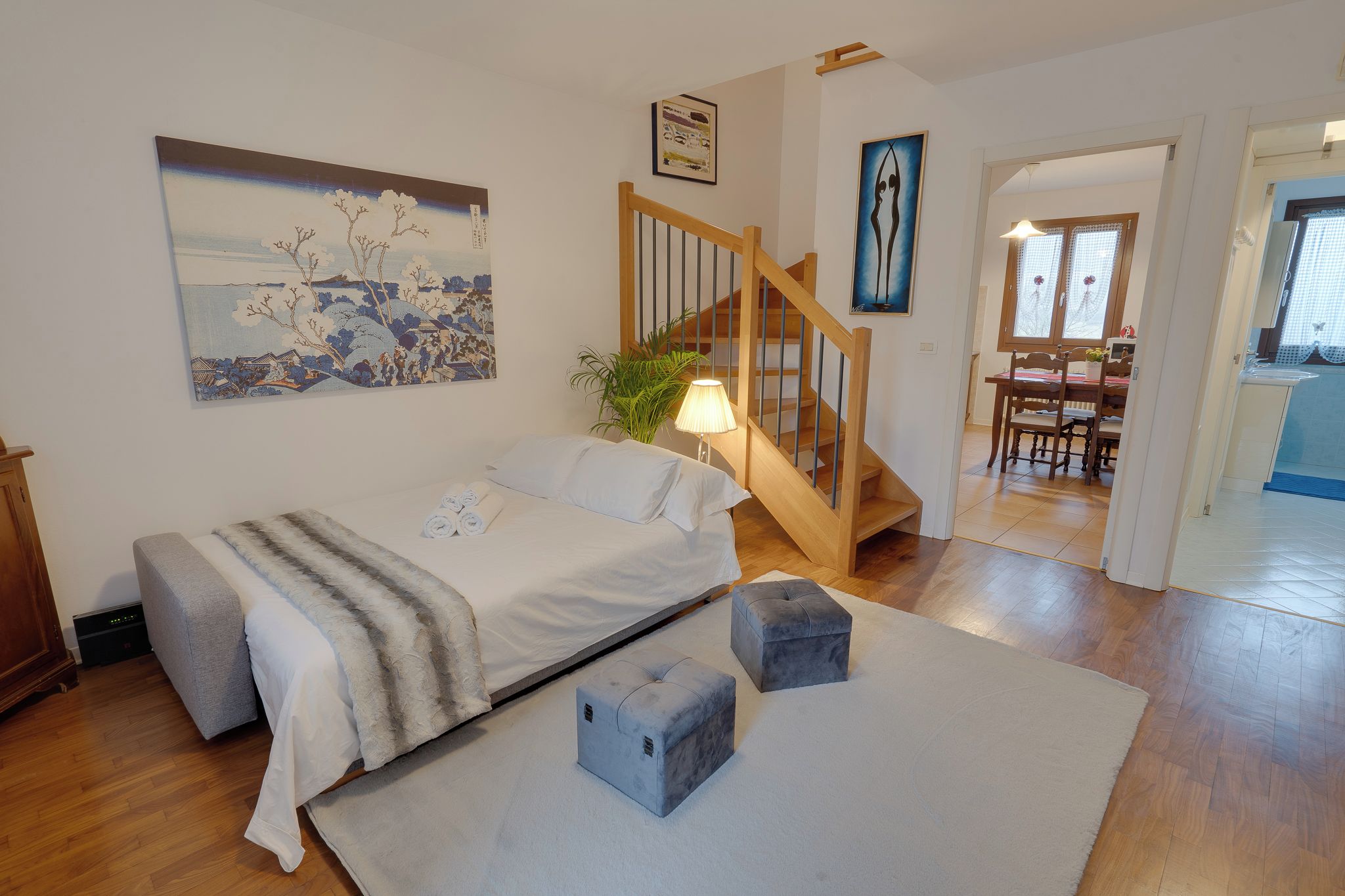 Un dormitorio con cama, mesita de noche, lámpara y un cuadro en la pared.