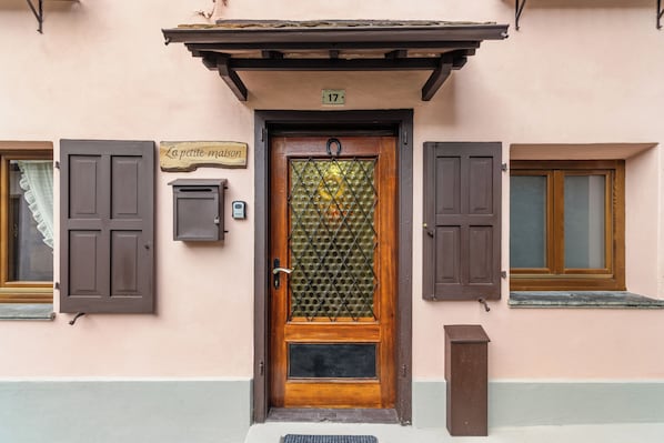 A building entrance with a wooden door, a sign above it, and two windows with shutters.