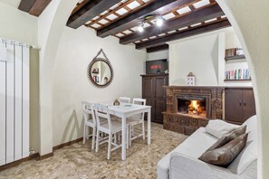 A cozy living room with a fireplace, a dining area with a table and chairs, and a bookshelf. - La Petite Maison - Near Zoncolan and Sappada (Rigolato)