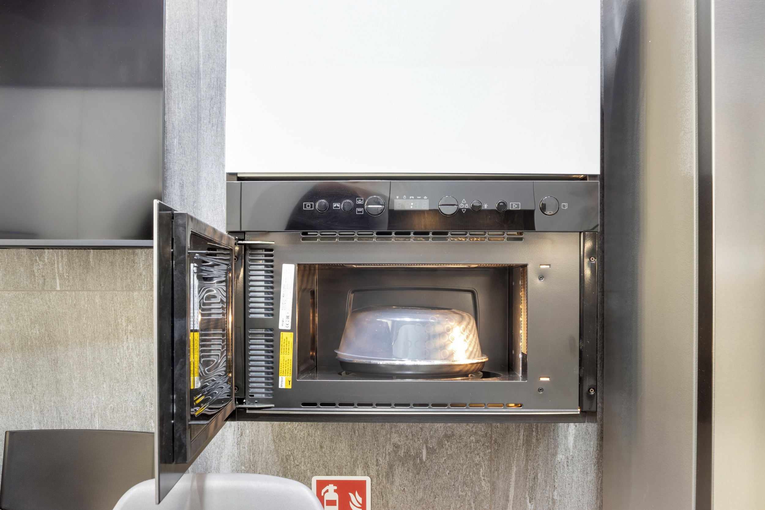 An outdoor oven with a digital control panel, a fire extinguisher, and a caution sign.