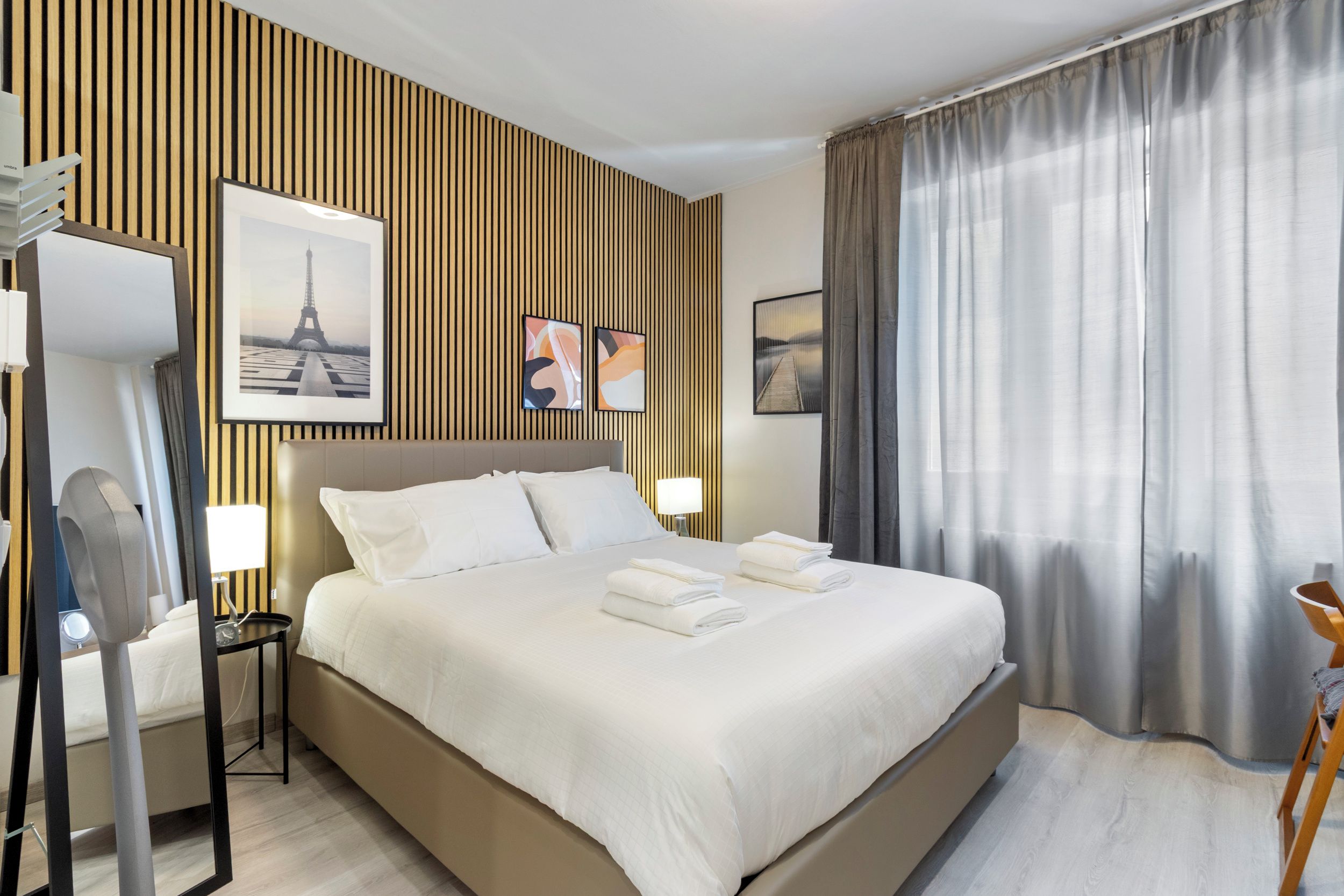 Ein Hotelzimmer mit einem großen Bett, einem Nachttisch mit Lampe, einem Spiegel und Holzvertäfelung.