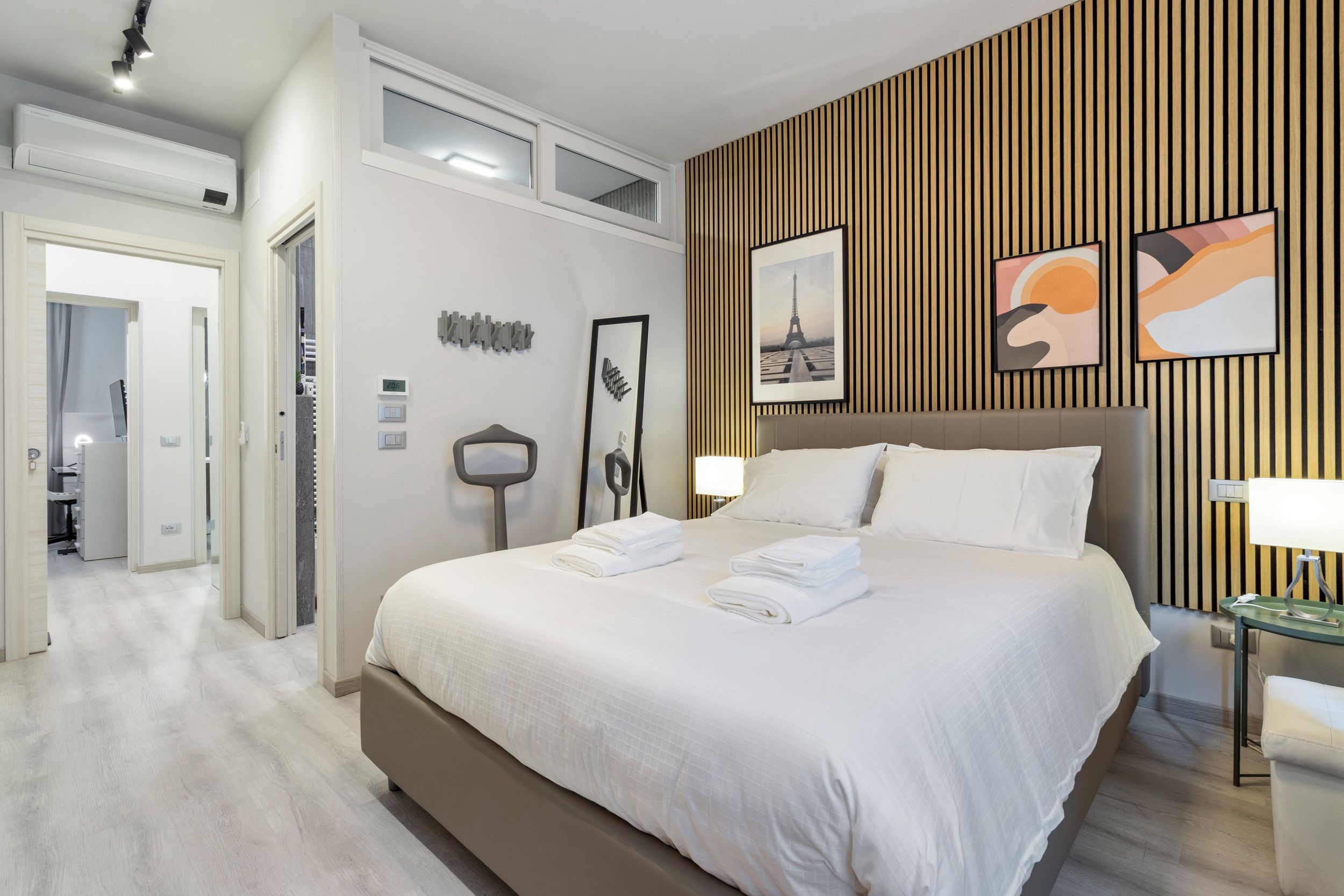 Habitación de hotel con una cama grande, un panel de pared de madera y obras de arte.