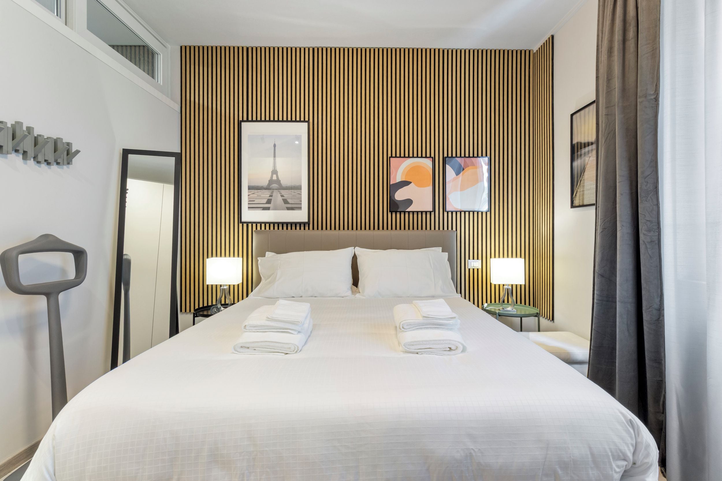 Une chambre d’hôtel avec un grand lit, deux tables de chevet, un miroir et une vue sur la Tour Eiffel.