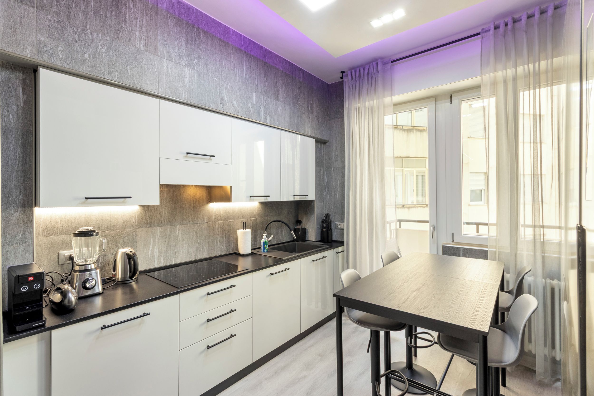 A modern kitchen with white cabinets, a black countertop, and a dining area with a table and chairs.