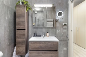 Et moderne badeværelse med en trækommode, et stort spejl, en indbygget varmeblæser og et toilet.
