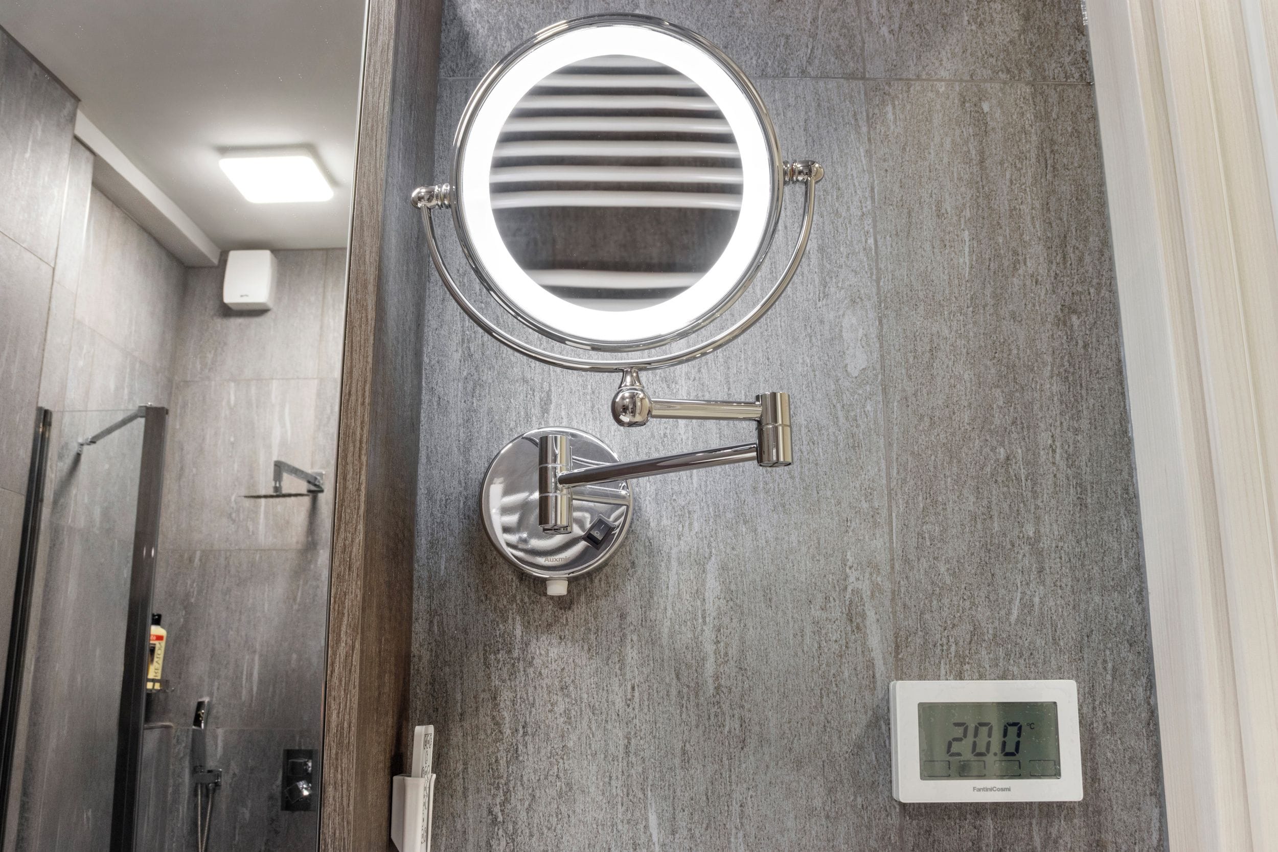 Un baño con un espejo redondo, un grifo de pared y una pantalla digital que muestra la temperatura.