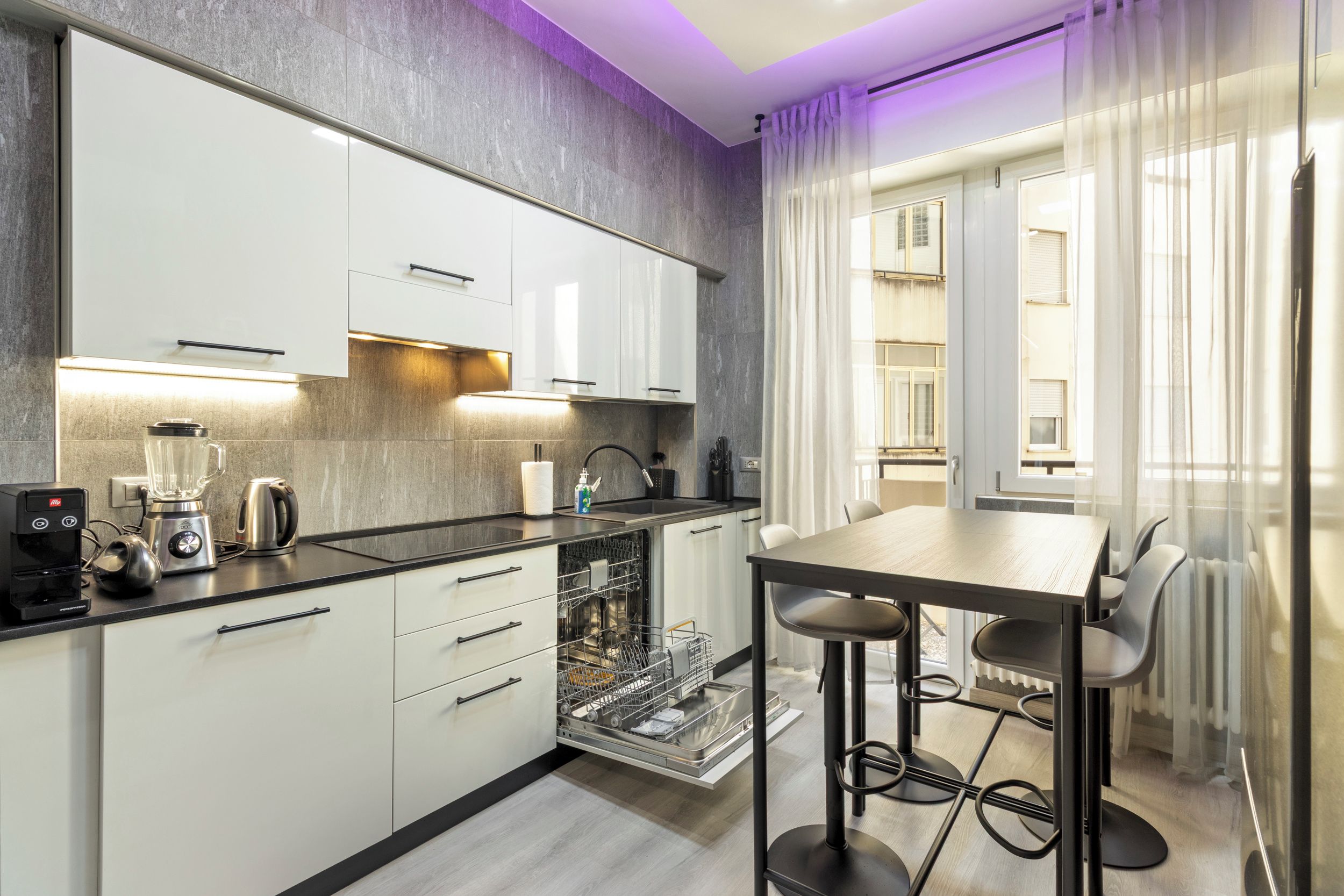 A modern kitchen with white cabinets, a built-in dishwasher, and a coffee machine.