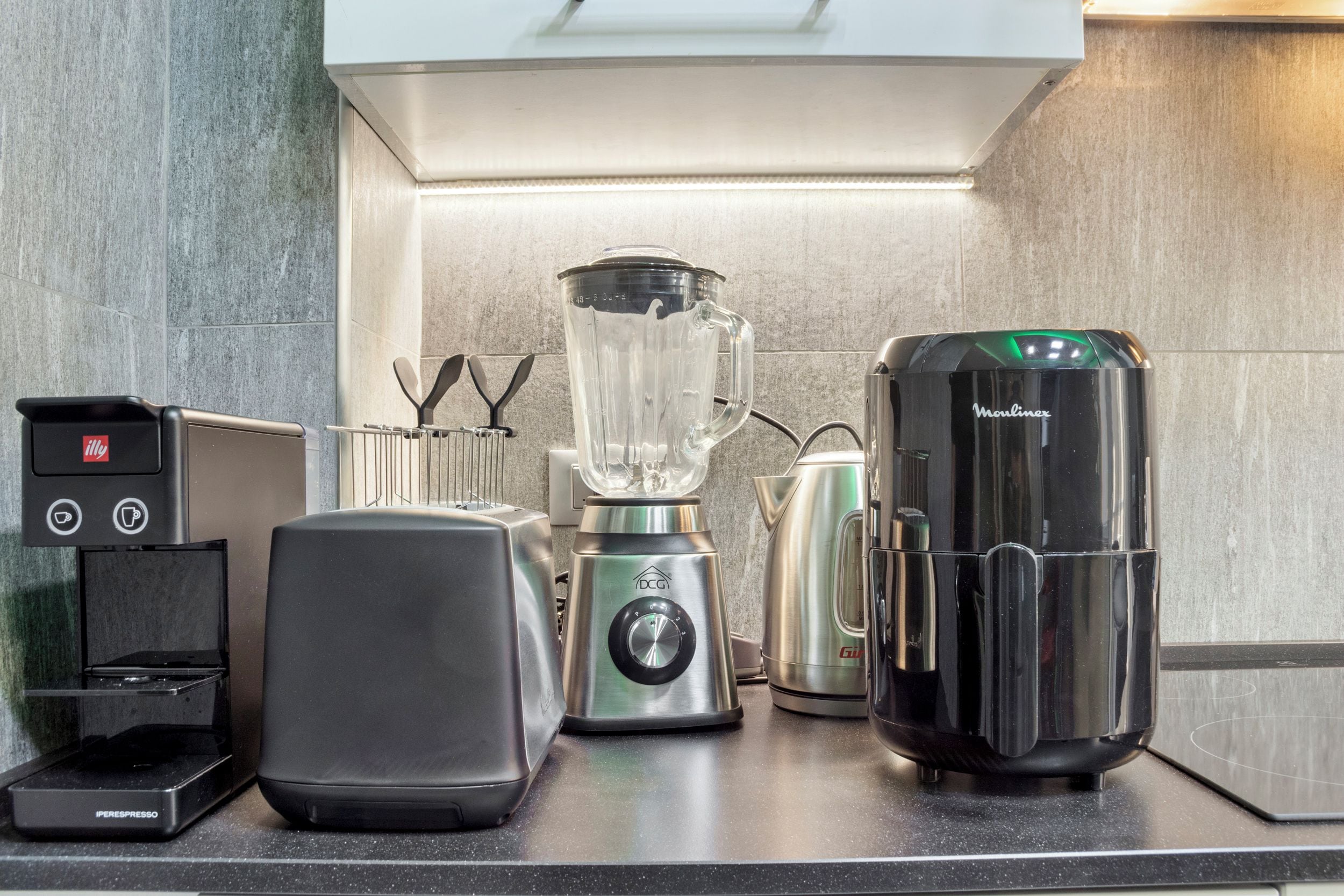 Una cucina con macchina del caffè, frullatore, bollitore e moka.
