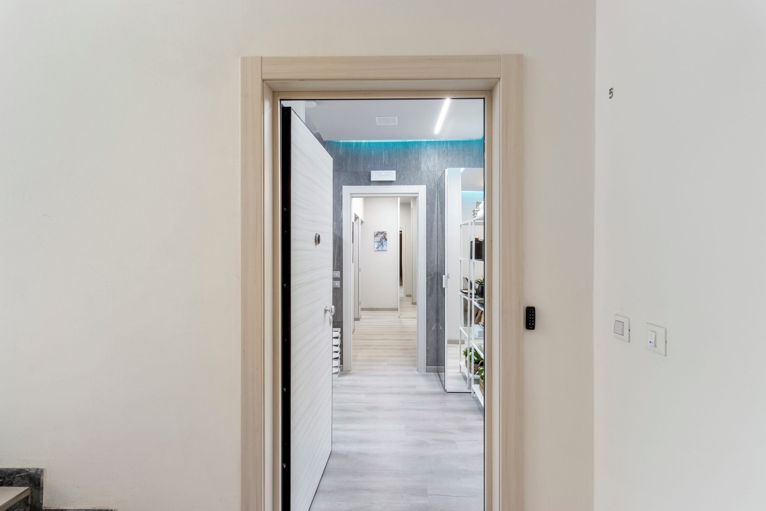 Un couloir avec une porte donnant sur une pièce dont un mur est blanc et un autre est d’une couleur bleue vive.