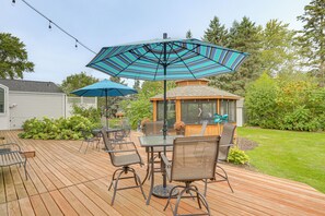 An outdoor patio with a wooden deck, a table with chairs, and a large striped umbrella. - New! Private Lakefront Retreat on Lindstrom Lake (Lindstrom)