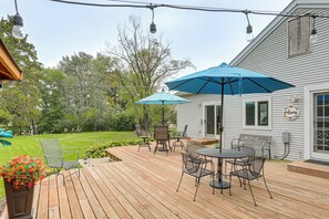 A wooden deck with outdoor furniture, including a table and chairs, and two blue umbrellas providing shade. - New! Private Lakefront Retreat on Lindstrom Lake (Lindstrom)