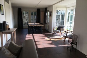 A living room with a sofa, a dining table, and chairs. There is a window providing natural light. - Holiday home with 3 bedrooms (Burgh-Haamstede)