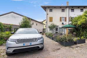 Un Range Rover était garé devant un immeuble, sur une allée dallée, entouré de plantes en pot et d’un petit espace aménagé pour s’asseoir à l’extérieur.