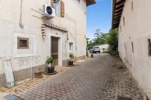 A narrow cobblestone street with buildings on either side, a parked car, and potted plants.