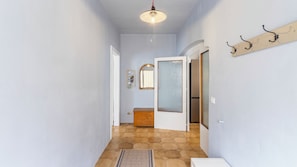 Un couloir avec un sol carrelé, un banc en bois, un miroir et un luminaire.