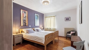 Ein Schlafzimmer mit einem hölzernen Bett, Nachttischen, einem Sessel und Bildern an den Wänden.