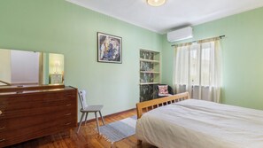 A bedroom with a bed, dresser, chair, shelves, and an air conditioning unit.