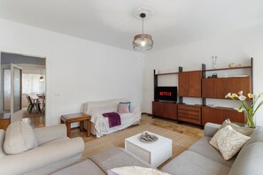 Ein modernes Wohnzimmer mit einer Couch, einem Couchtisch und einem Fernseher, der 'NETFLIX' anzeigt.
