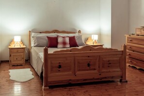 A wooden bed with a headboard, two bedside tables with lamps, a wooden dresser, and a white rug on a wooden floor. - Wooden Stories - Netflix, Wi-fi, Pet Friendly (Socchieve)