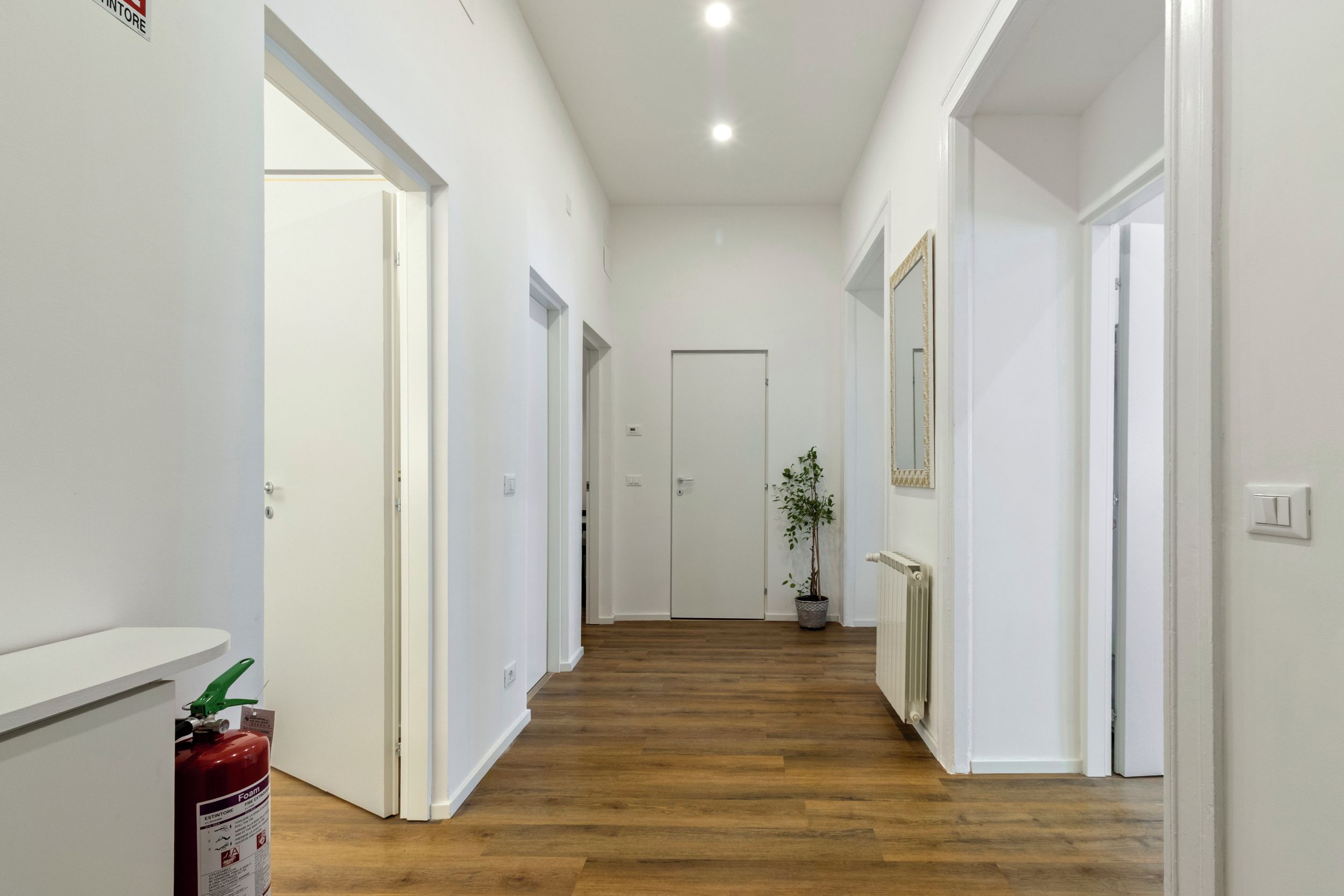 Un couloir aux murs blancs, doté d’un plancher en bois et de portes donnant sur d’autres pièces.