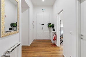 A hallway with white walls, wooden flooring, a white door at the end, and a fire extinguisher mounted on the wall. - Tiffany - Netflix, Disney, per 8pp con Garage Box (Trieste)