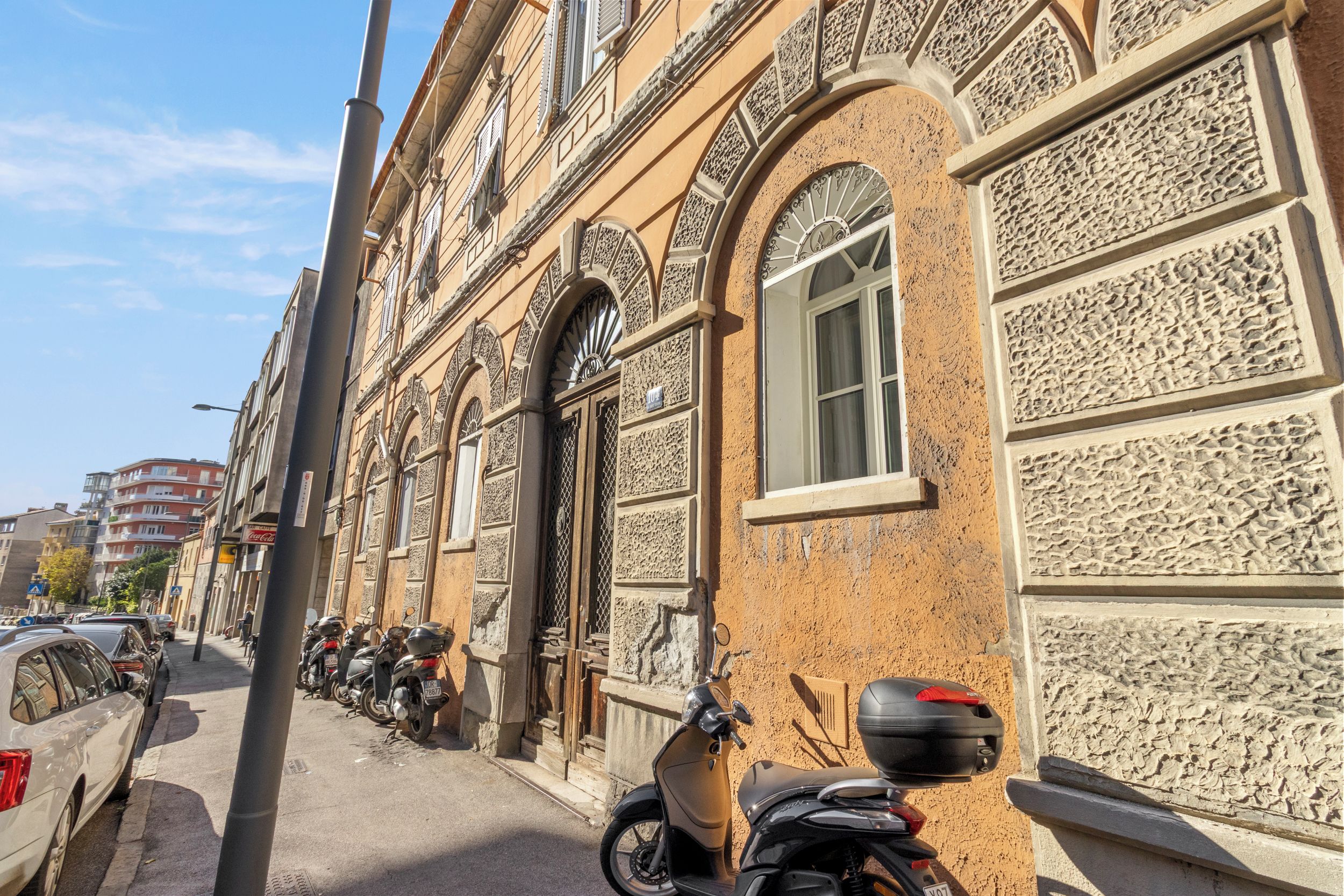 A street with parked motorcycles and cars, buildings with ornate facades, and a clear sky.