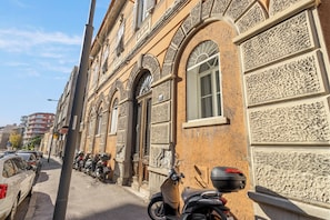 A street with parked motorcycles and cars, buildings with ornate facades, and a clear sky. - Tiffany - Netflix, Disney, per 8pp con Garage Box (Trieste)