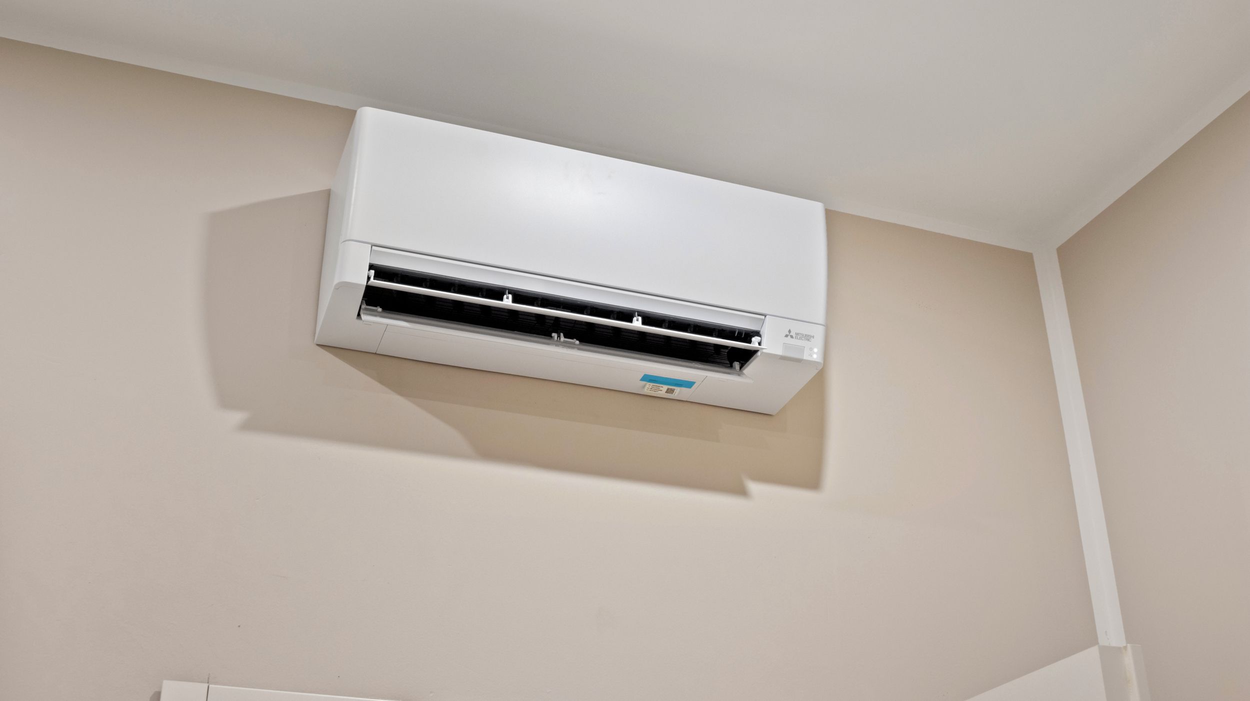 A white air conditioning unit mounted on a wall in a room with plain walls.