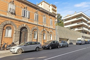 A street with parked cars and a building with arched windows and a stone facade. - Tiffany - Netflix, Disney, per 8pp con Garage Box (Trieste)