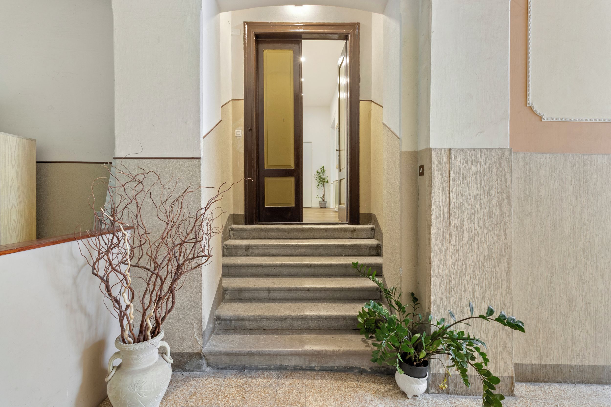 A staircase leading to a room with a door, a potted plant, and a vase with branches.