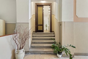 A staircase leading to a room with a door, a potted plant, and a vase with branches. - Tiffany - Netflix, Disney, per 8pp con Garage Box (Trieste)