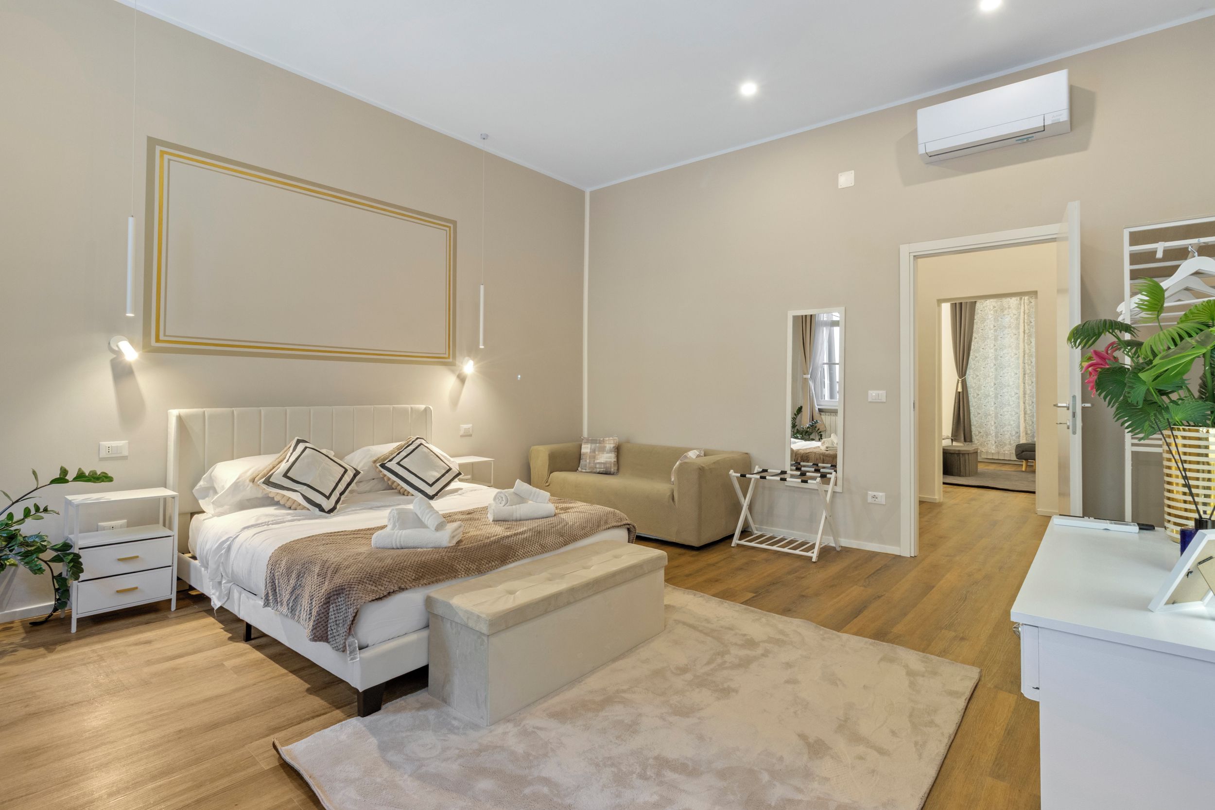 A modern bedroom with a bed, bedside tables, a bench, a mirror, and a wardrobe.