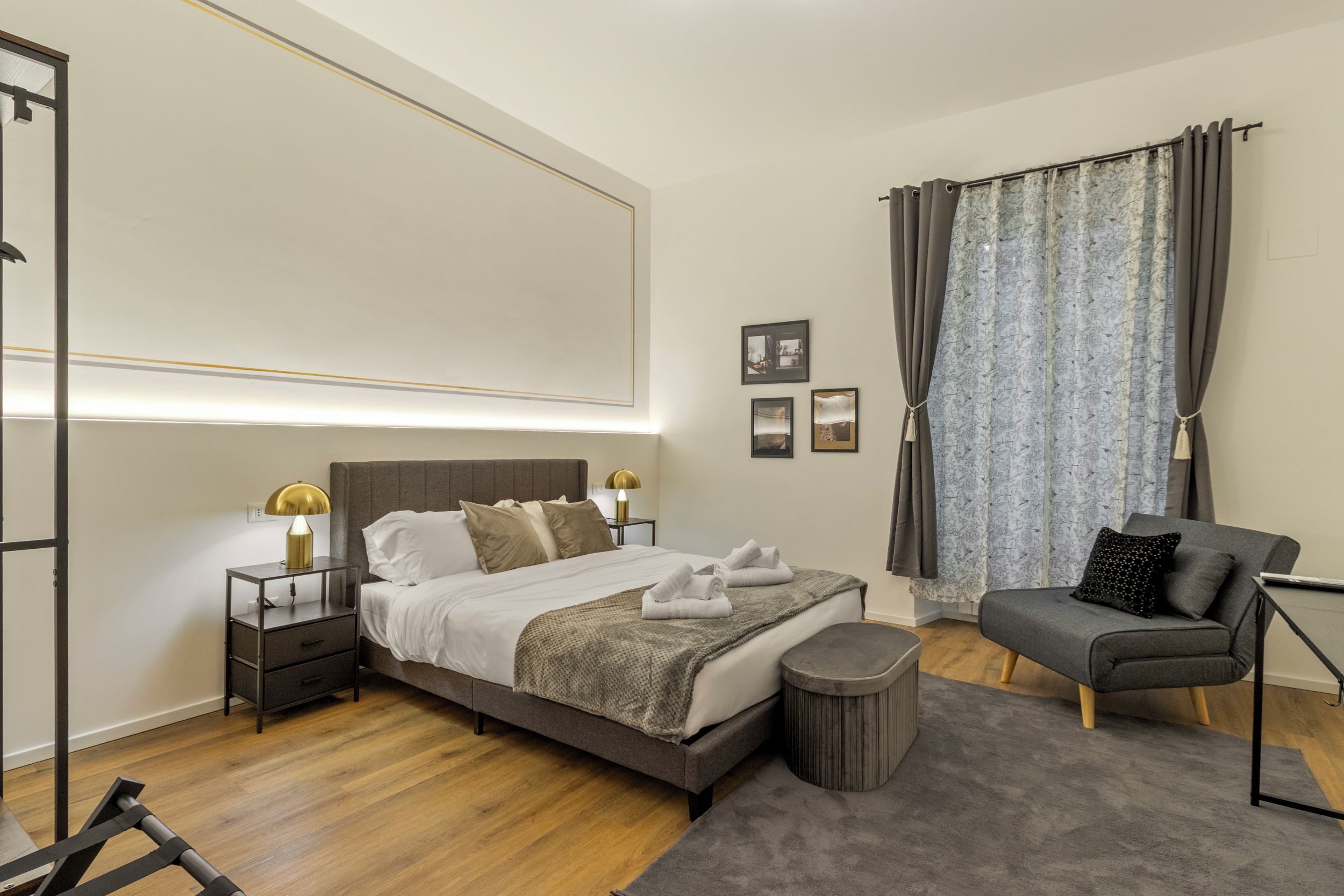 Une chambre moderne avec un lit, des tables de chevet, une chaise et un petit pouf rond.
