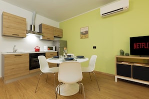 A modern kitchen with wooden cabinets, a built-in oven, and a dining area with white chairs and a table set for two. - New! Tocai in via Rastello per 4 pp (Gorizia)