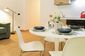Zona de menjador moderna amb una taula rodona per a quatre, cadires blanques i cuina al fons.