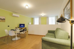 A living room with a green sofa, a dining table with chairs, a TV, and a lamp. - New! Tocai in via Rastello per 4 pp (Gorizia)