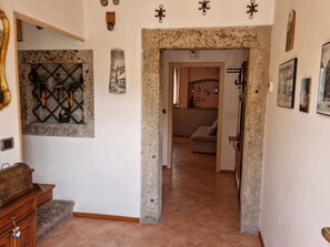 A hallway with a stone archway leading to a living area with a sofa and a wall decorated with various items.