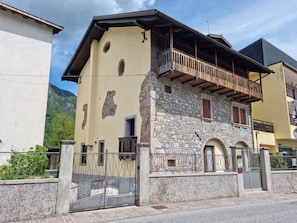 A two-story building with a stone facade, wooden balcony, and a gated entrance. - La Cjase di Tacuin - Dimore Tipiche Friulane (Ampezzo)