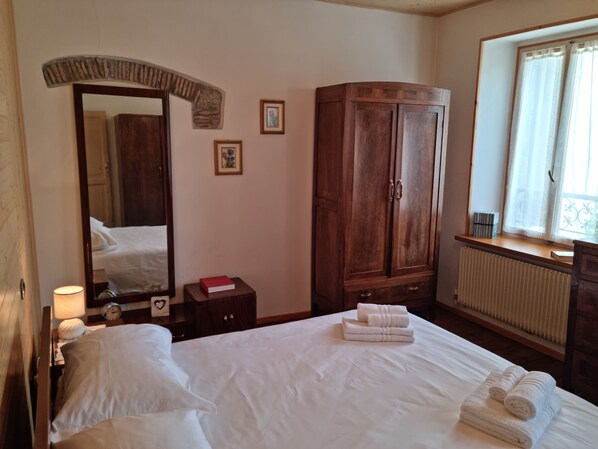 A hotel room with a bed, a wardrobe, a mirror, a bedside table with a lamp, and a window with a view.