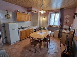 A kitchen with wooden cabinets, a refrigerator, a sink, and a dining table with chairs.