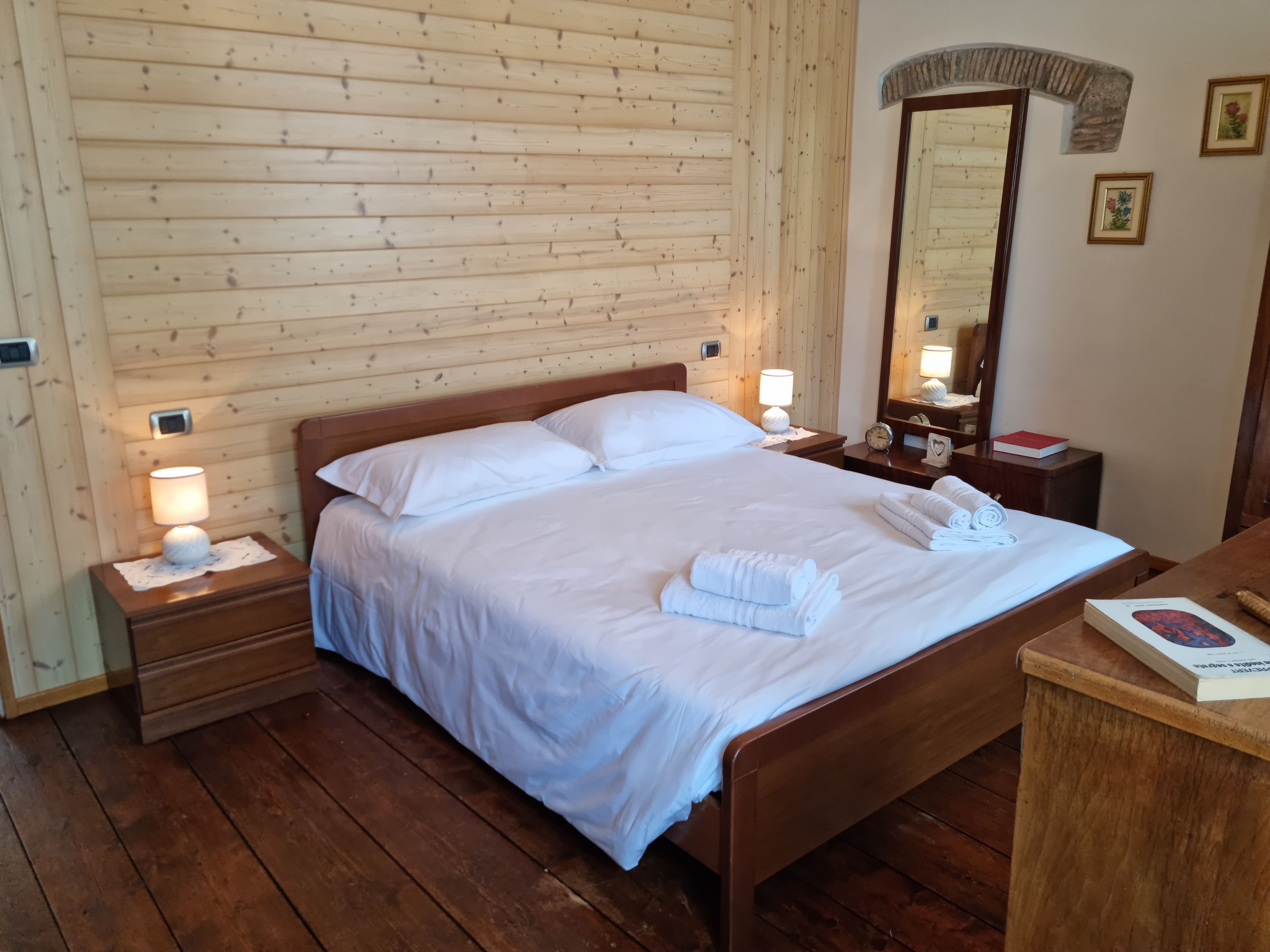 Ein Zimmer mit Holzwänden, einem Bett, Nachttischen, einem Spiegel und einer Holzkommode.