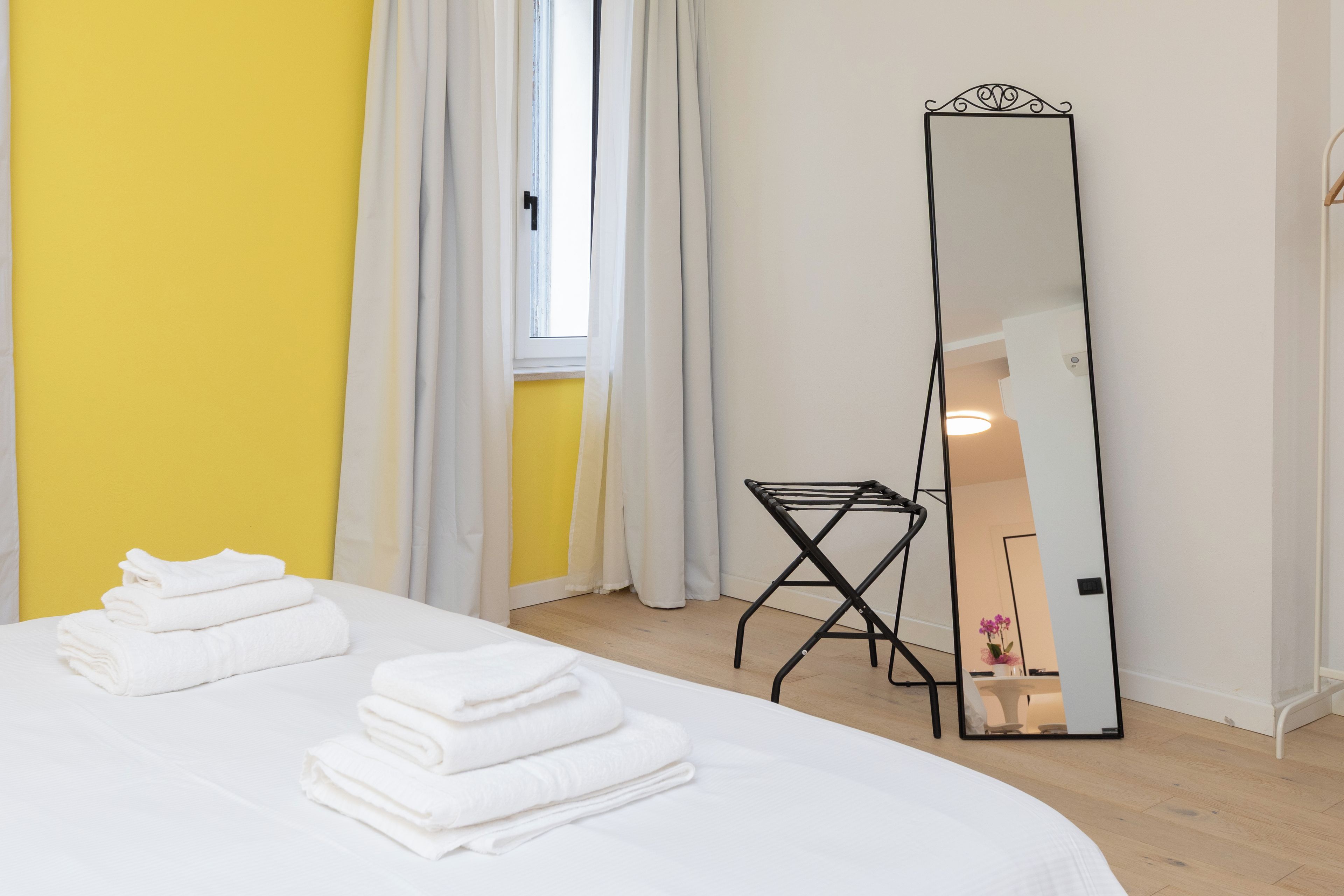 Een hotelkamer met een bed, een spiegel, een raam met gordijnen en een klein tafeltje.